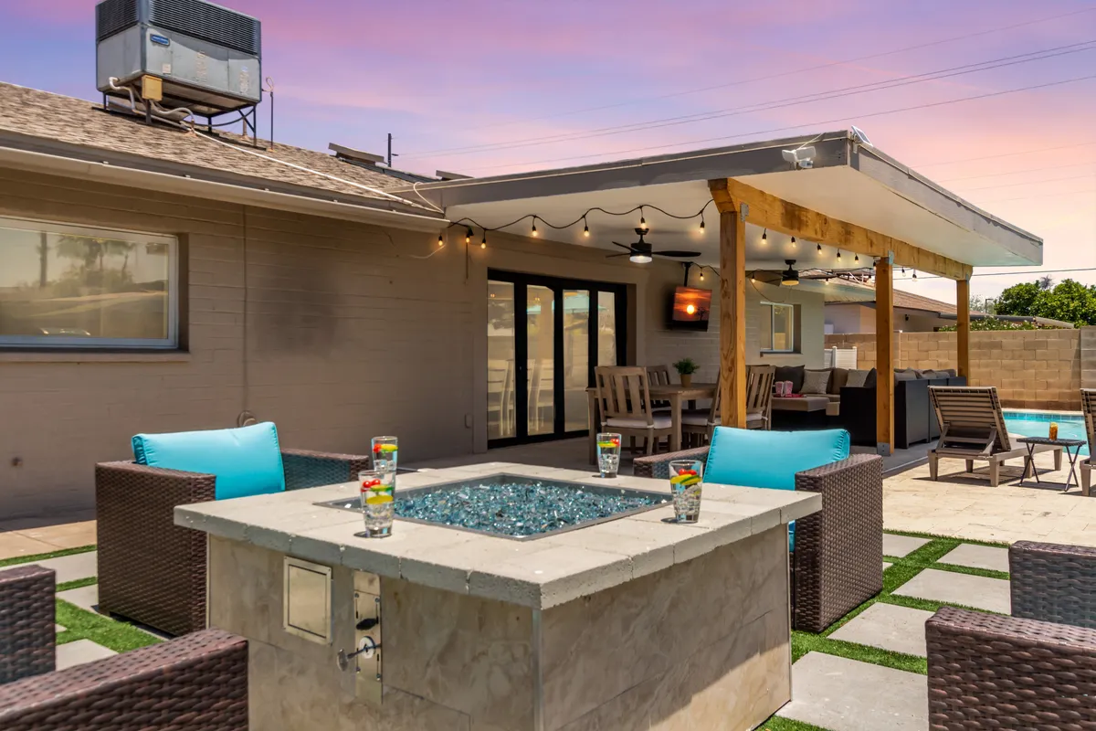 A welcoming outdoor entertainment space with a fire pit surrounded by comfortable seating, an outdoor kitchen with a grill, and the turquoise pool in the background. The setting is perfect for both social gatherings and tranquil evenings by the fire.