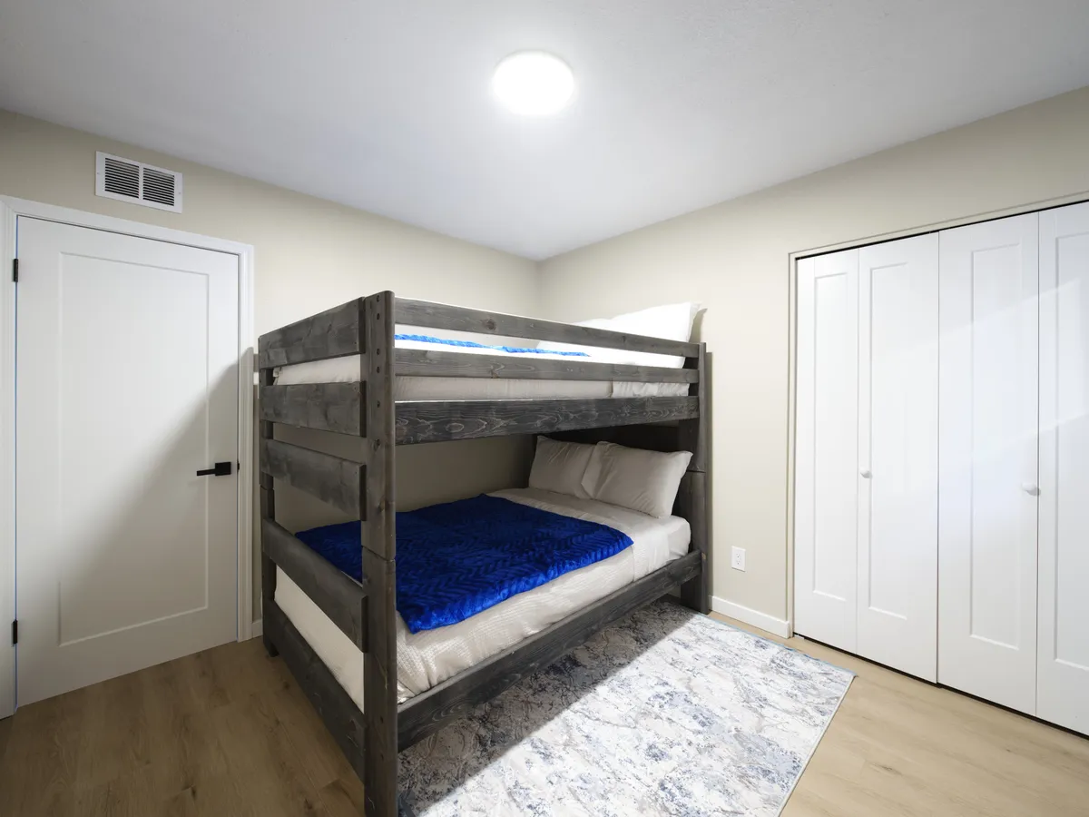 A charming bunk bed setup complete with a cozy area rug and closet doors nearby. The playful arrangement is ideal for children or friends sharing a space and exudes a sense of fun and togetherness.