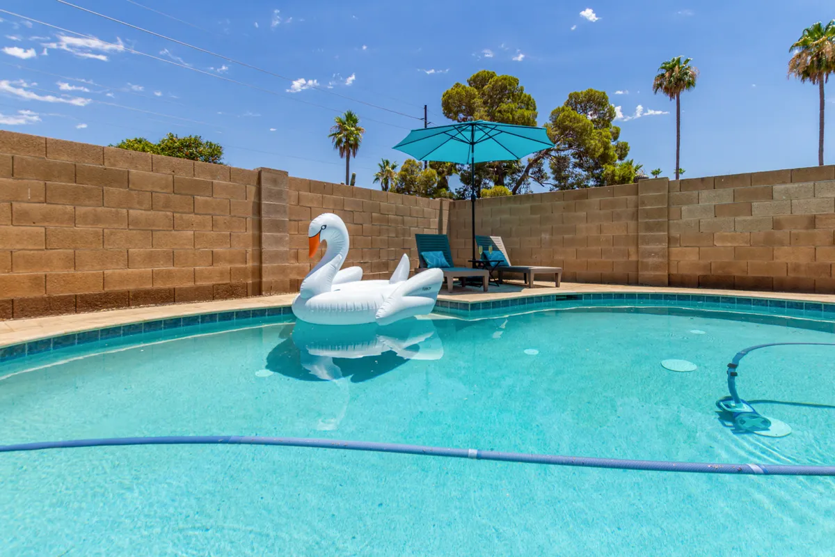 This exterior shot captures a sparkling swimming pool with an inflatable swan, umbrella, and lounge chairs. The sun is setting, casting a warm glow over the inviting outdoor space, perfect for relaxing or entertaining.
