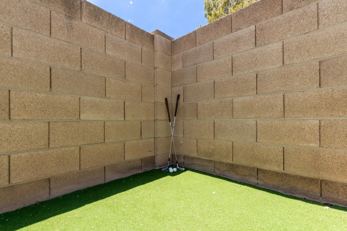 A dedicated putting green area with golf clubs and balls laid out on vibrant artificial grass, bordered by brick walls. The scene invites guests to practice their swing in a playful, resort-like setting.