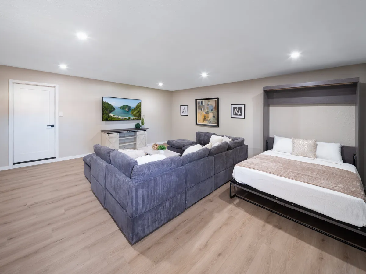 A spacious living area with a sectional sofa that converts into a fold-out bed, complemented by a wall-mounted TV and decorative artwork. The setting is casual and ideal for hosting or accommodating additional guests.
