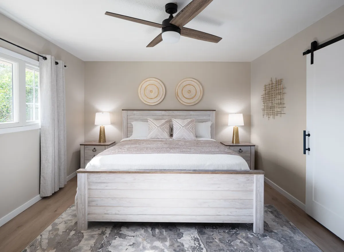 A tranquil bedroom featuring a neatly made bed with decorative wall plates above the headboard, flanked by nightstands and lamps. A soft rug adds warmth to the space, and gentle lighting creates an inviting atmosphere ideal for relaxation and restful sleep.