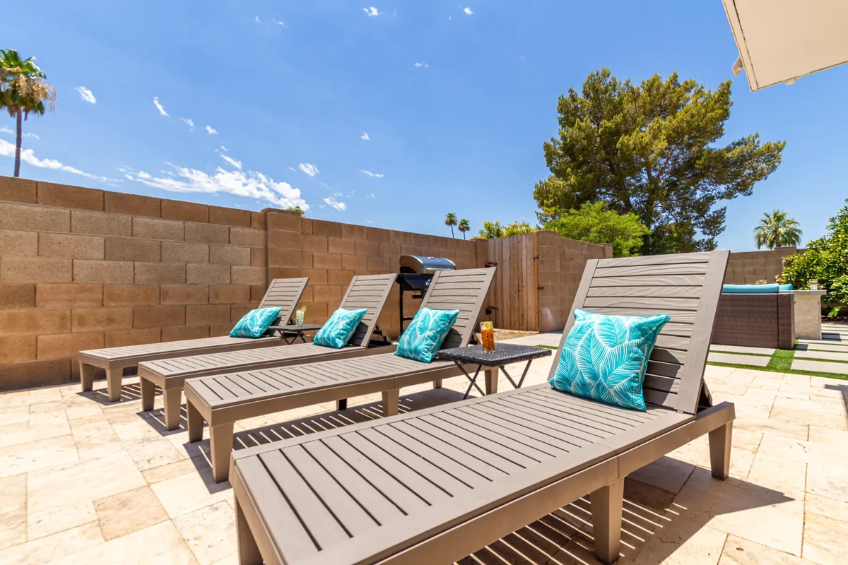 A tranquil yet social poolside area with lounge chairs, decorative pillows, a sparkling pool, and an outdoor grill, basked in sunset light. The space is clearly designed for group gatherings, sunbathing, barbecuing, and relaxed celebrations.