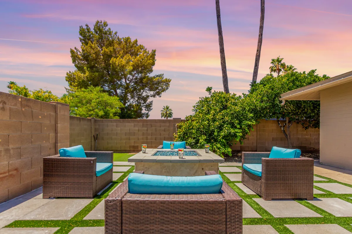 An outdoor seating area surrounds a fire pit, set amidst lush greenery with a vibrant sunset sky. The setup invites relaxed gatherings and cozy evenings under the desert stars, mirroring the resort-like ambiance described in the narrative.