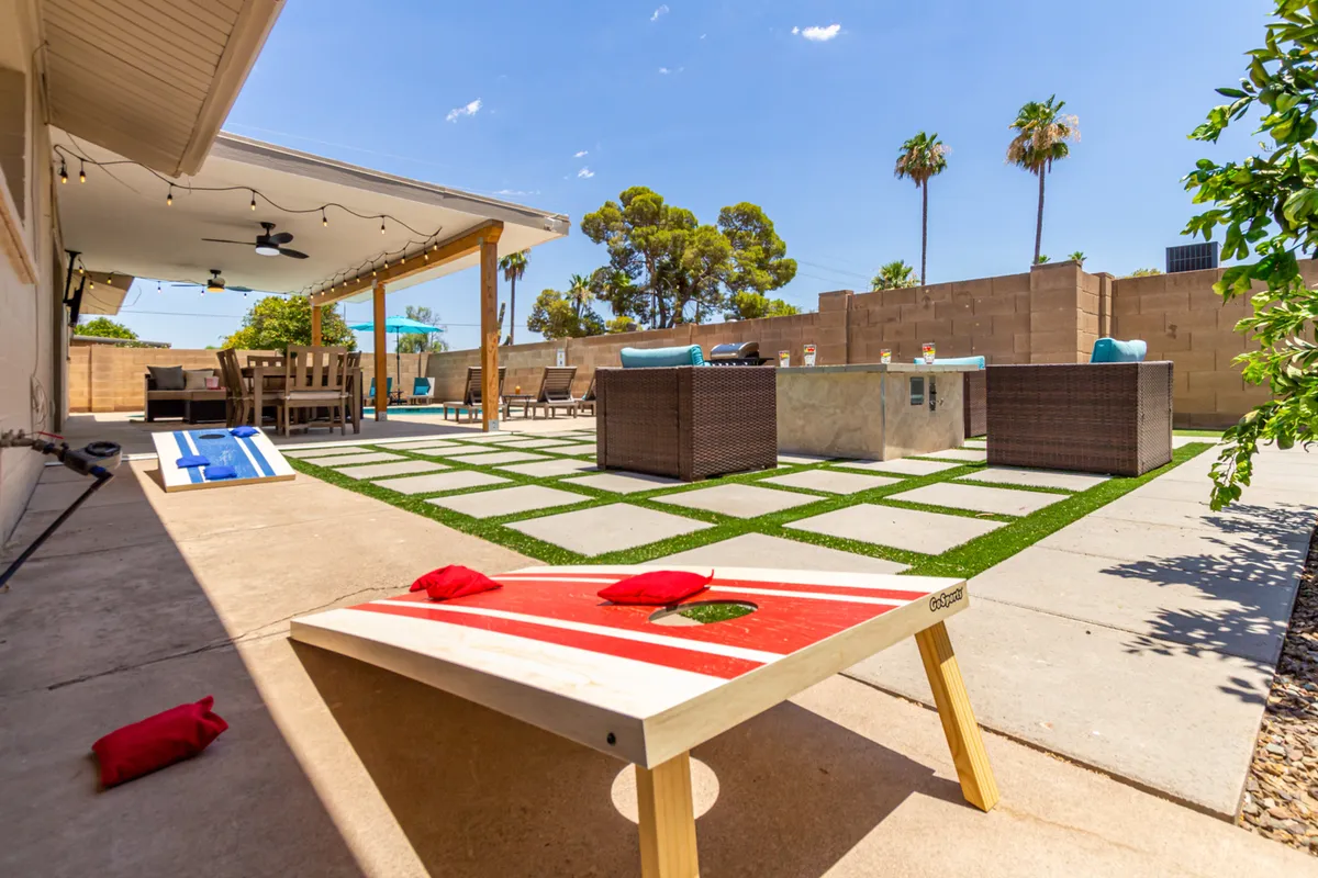 A cheerful backyard nook with a cornhole board set up on the lawn, a cozy sitting area, and lush plants, inviting guests to engage in friendly games or relax outdoors together.