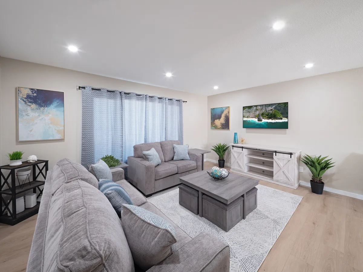 A cozy living area with comfortable gray sofas, decorative paintings on the wall, a TV with a scenic view, and a coffee table with a decorative bowl. The room exudes warmth, ideal for socializing, watching movies, or relaxing with friends and family.